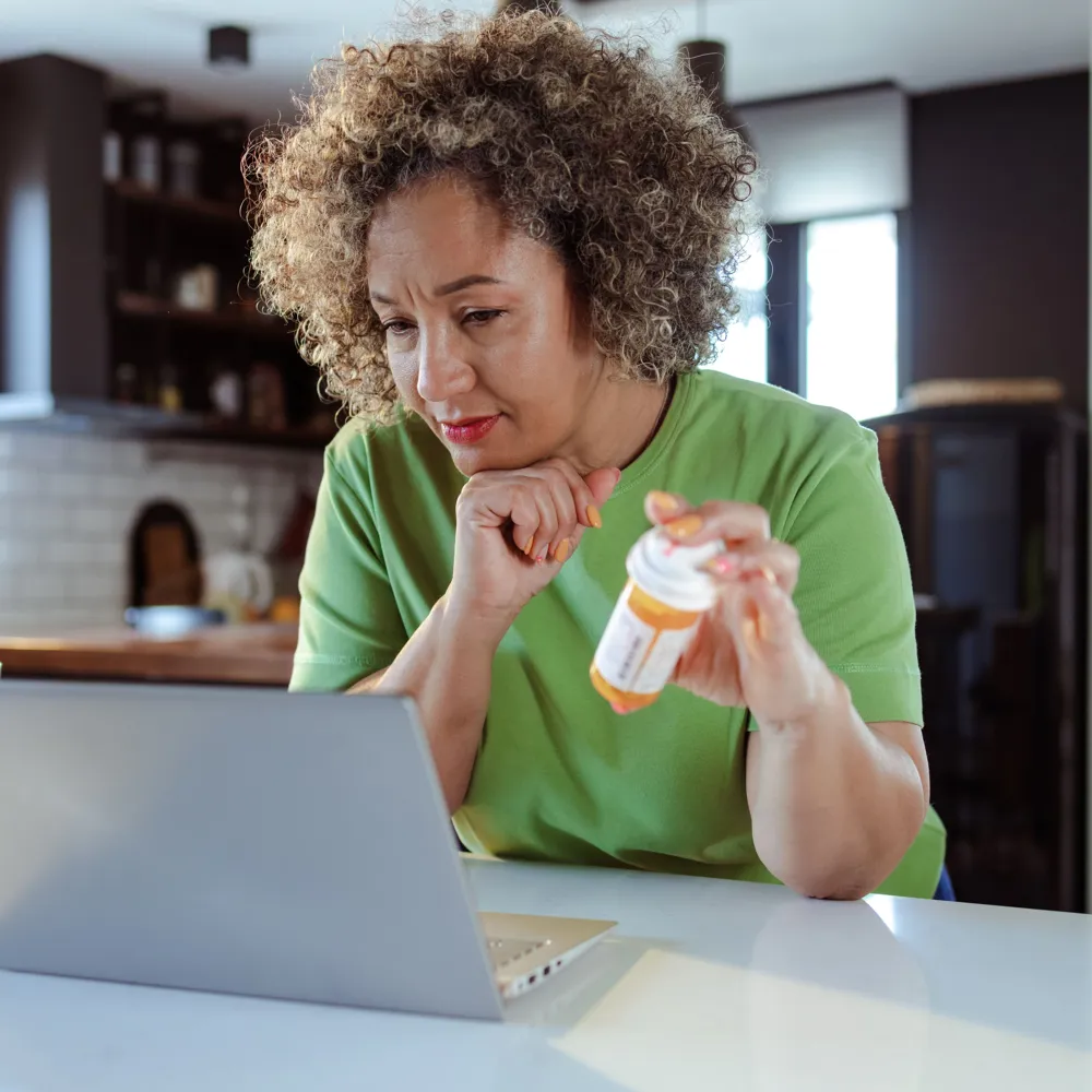 Alt Text: Women sitting at the table in the living room and searching information about medicine on the internet.