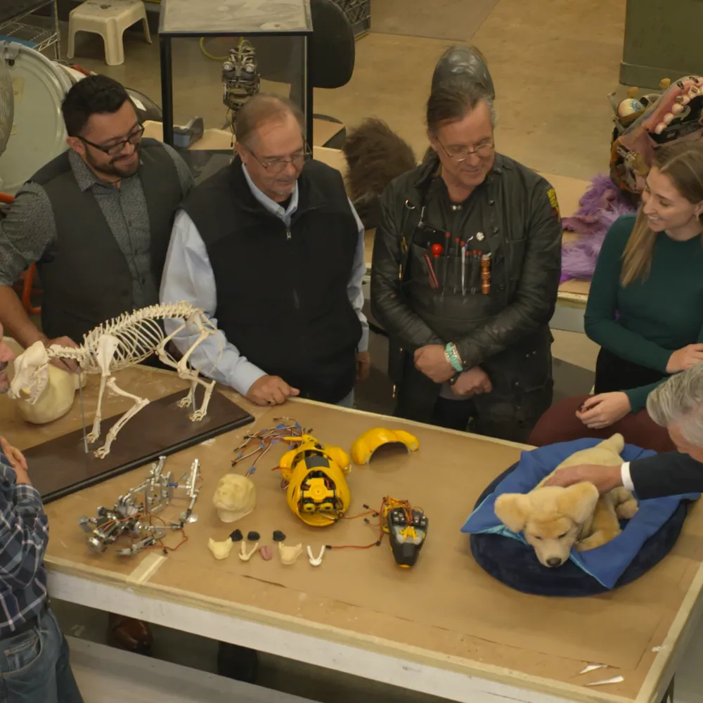 Alt Text: Tombot visits Jim Henson’s Creature Shop to update the look of Tombot’s robotic emotional support companion puppy Jennie.