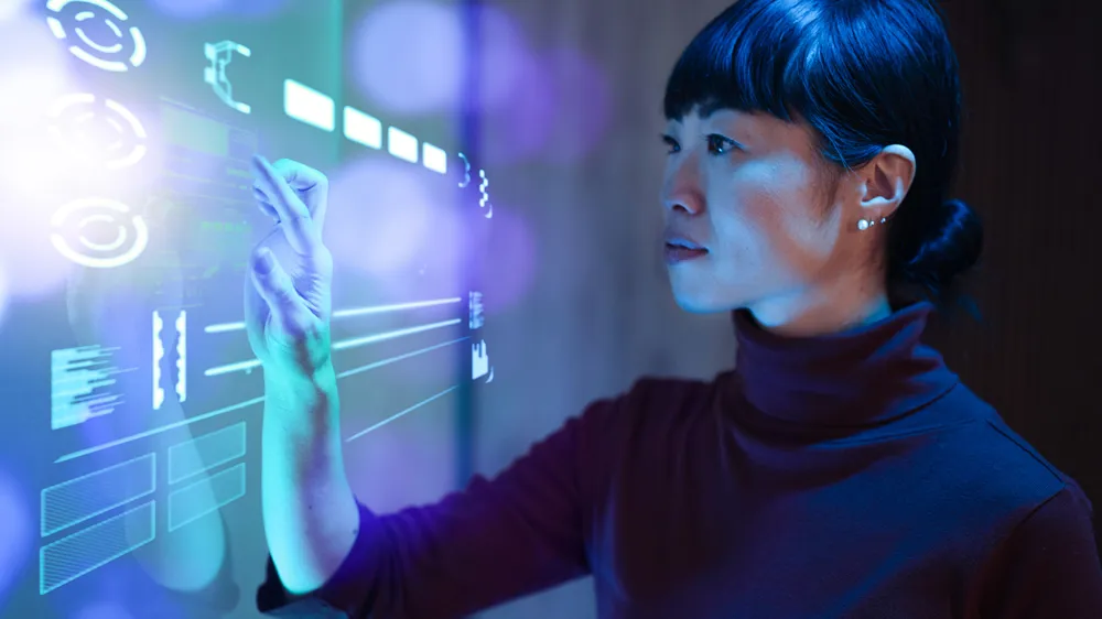 ALT Text: A person interacts with a holographic interface, touching virtual data and graphs, with a futuristic illuminated display.
