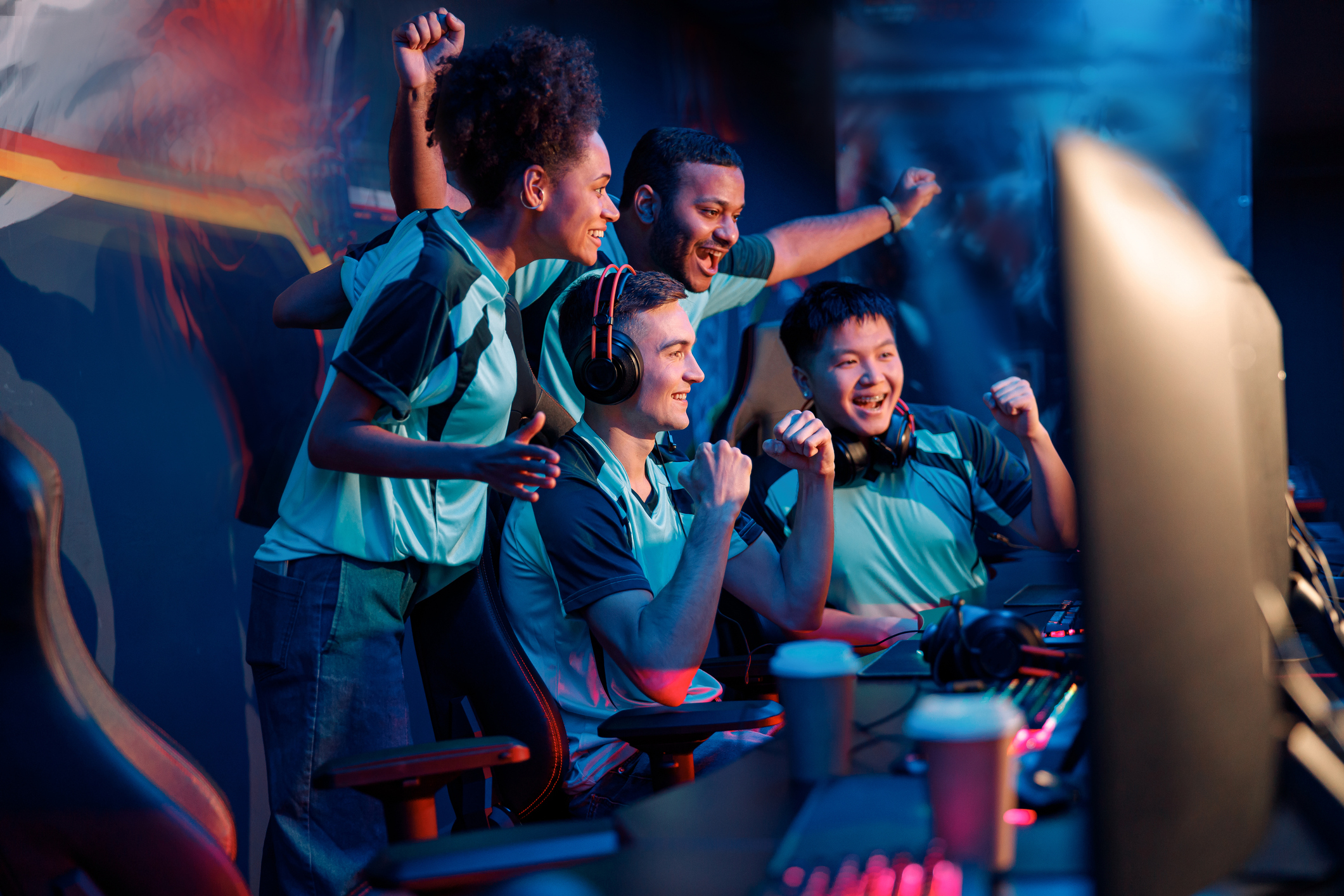ALT Text:  cybersport gamers expressing success while raising hands up and smiling during participation in esports tournament in computer club