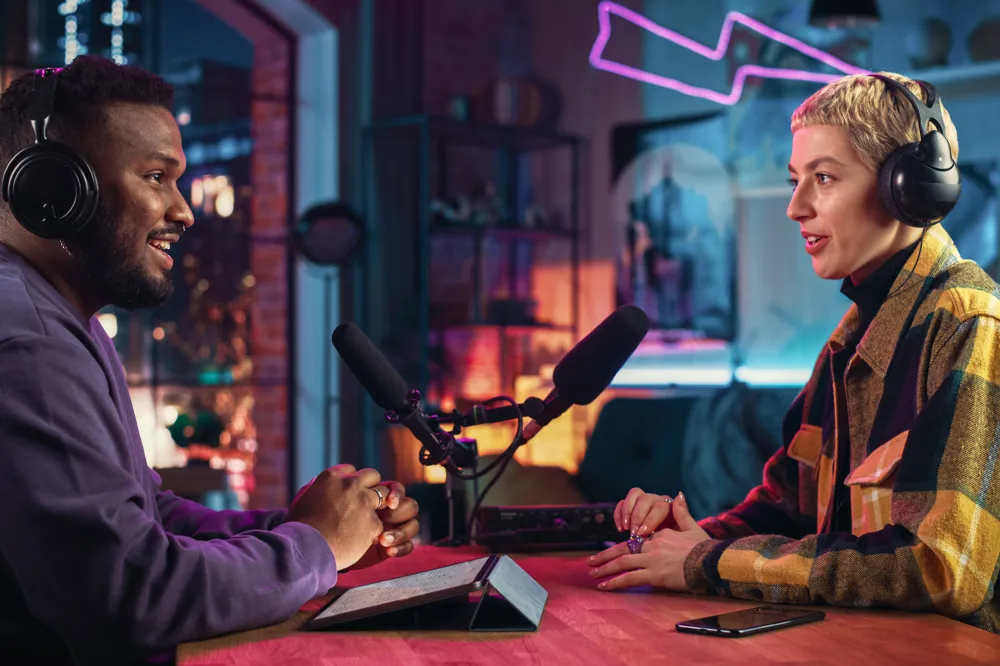 ALT Text: Two Young Stylish Radio Show Hosts Record Fresh Podcast Episode in Home Loft Studio Apartment. Attractive Energetic Co-hosts Discuss Important Topics Live on Air in an Evening Show.