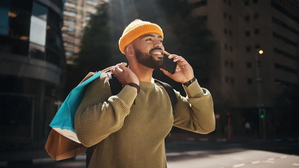 Alt Text: Man, phone call and shopping in city with travel, walking and talking of student deal, discount or online sale in street