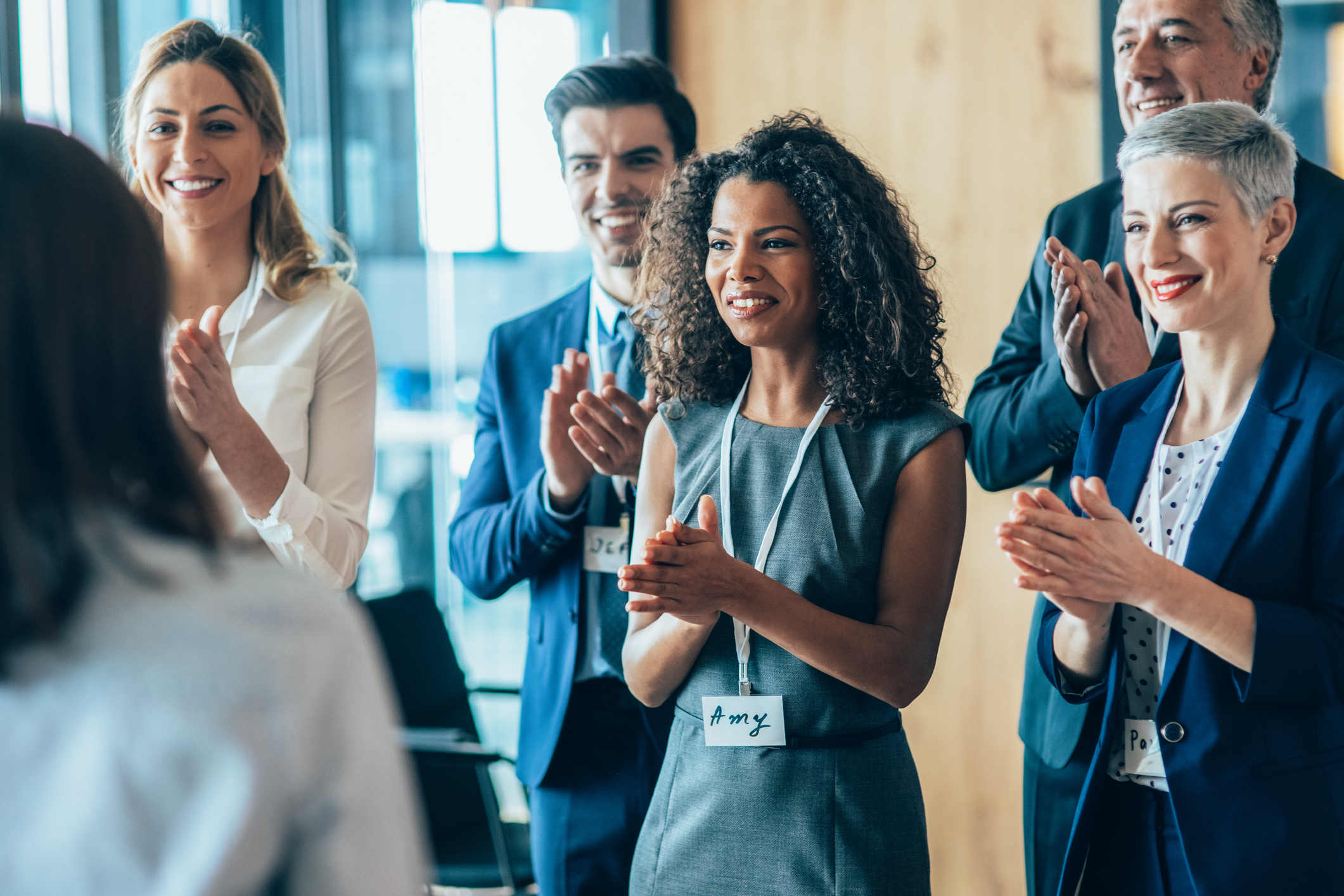 Alt Text: Smiling audience applauding at a business seminar. Group of business people standing and applauding.
